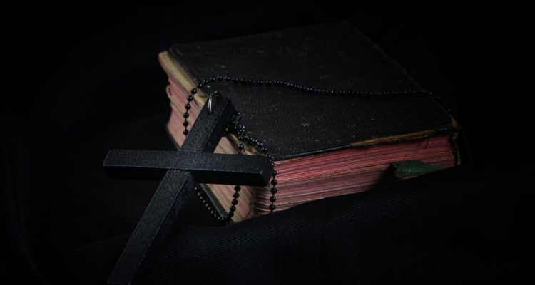 black cross leaning on black hardcover bible